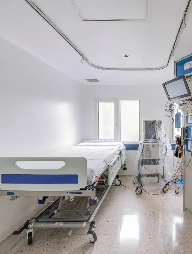 Cama hospitalaria en sala blanca equipada para atención de pacientes.